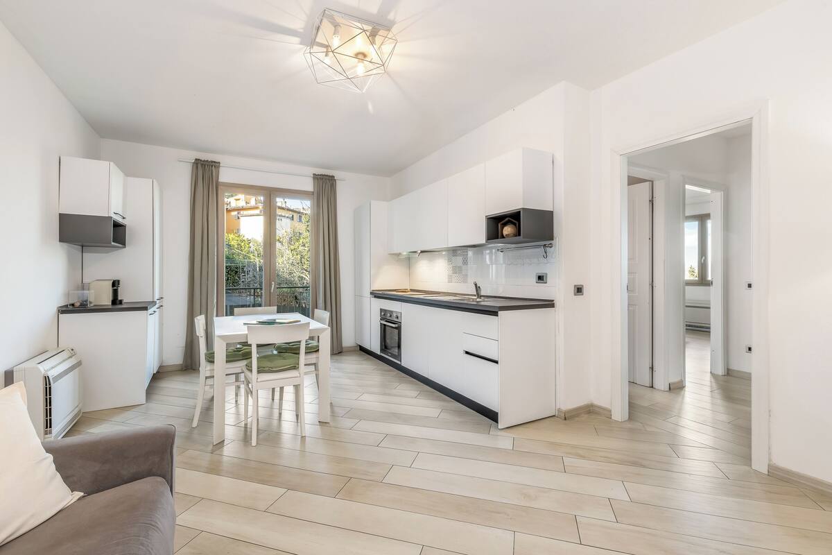 A modern kitchen with white cabinetry, a dining area with a table and chairs, and a living area with a sofa.