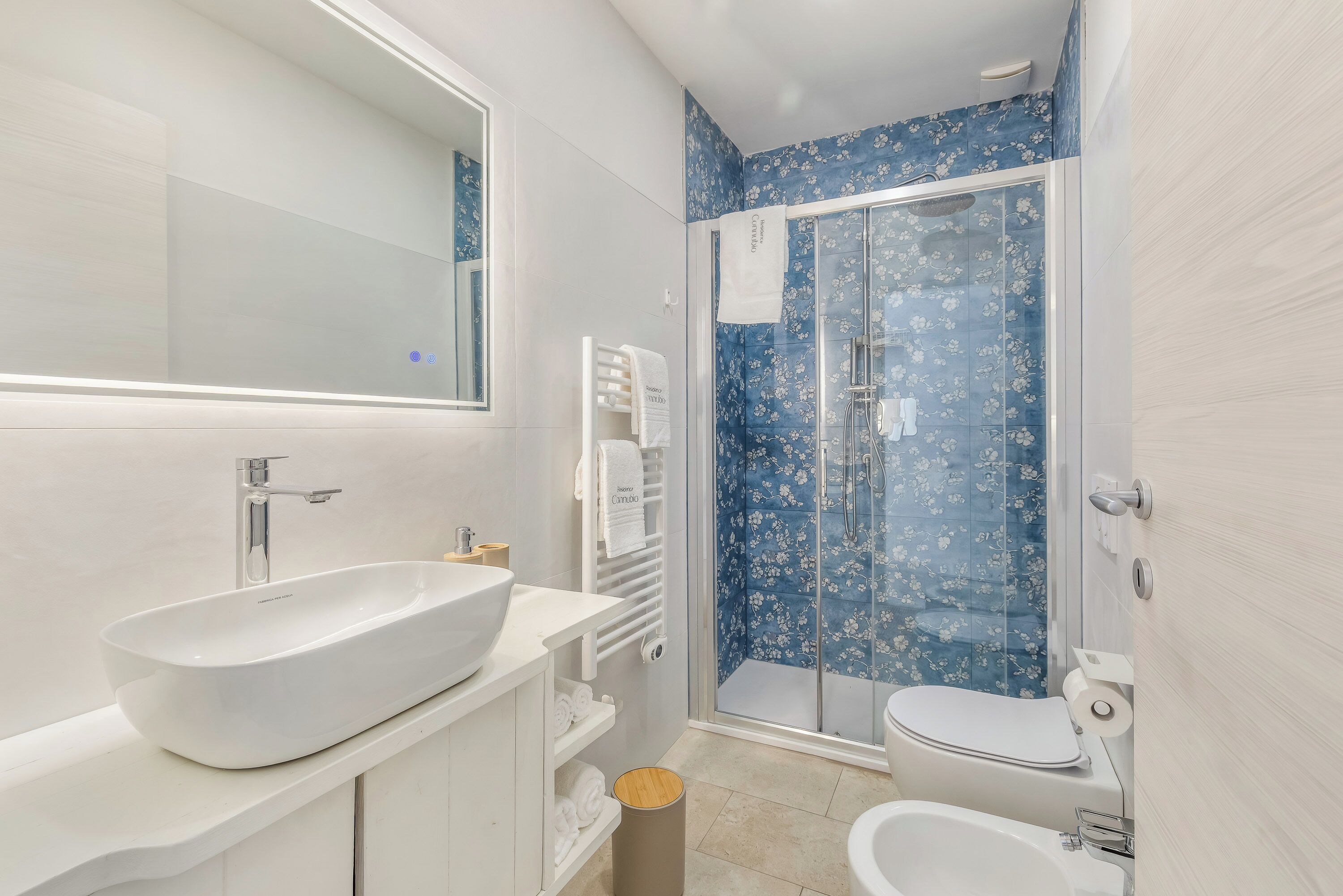 Un baño con un lavamanos grande blanco, un inodoro, un bidé y una ducha con puerta de cristal.