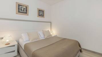A neatly made bed with a beige blanket, a white headboard, and two bedside lamps.