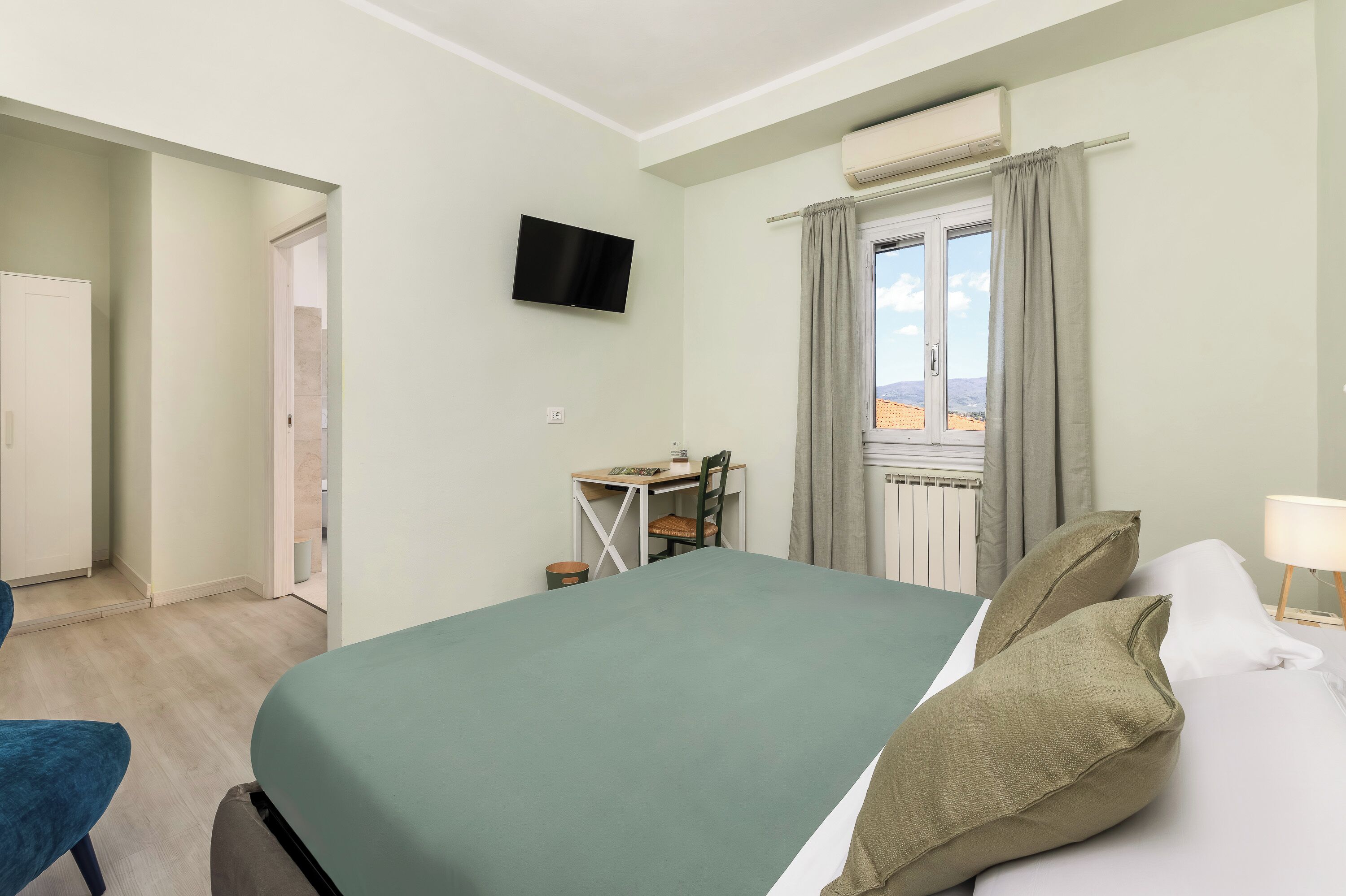 A hotel room with a bed, a desk, a television, and a window with curtains.