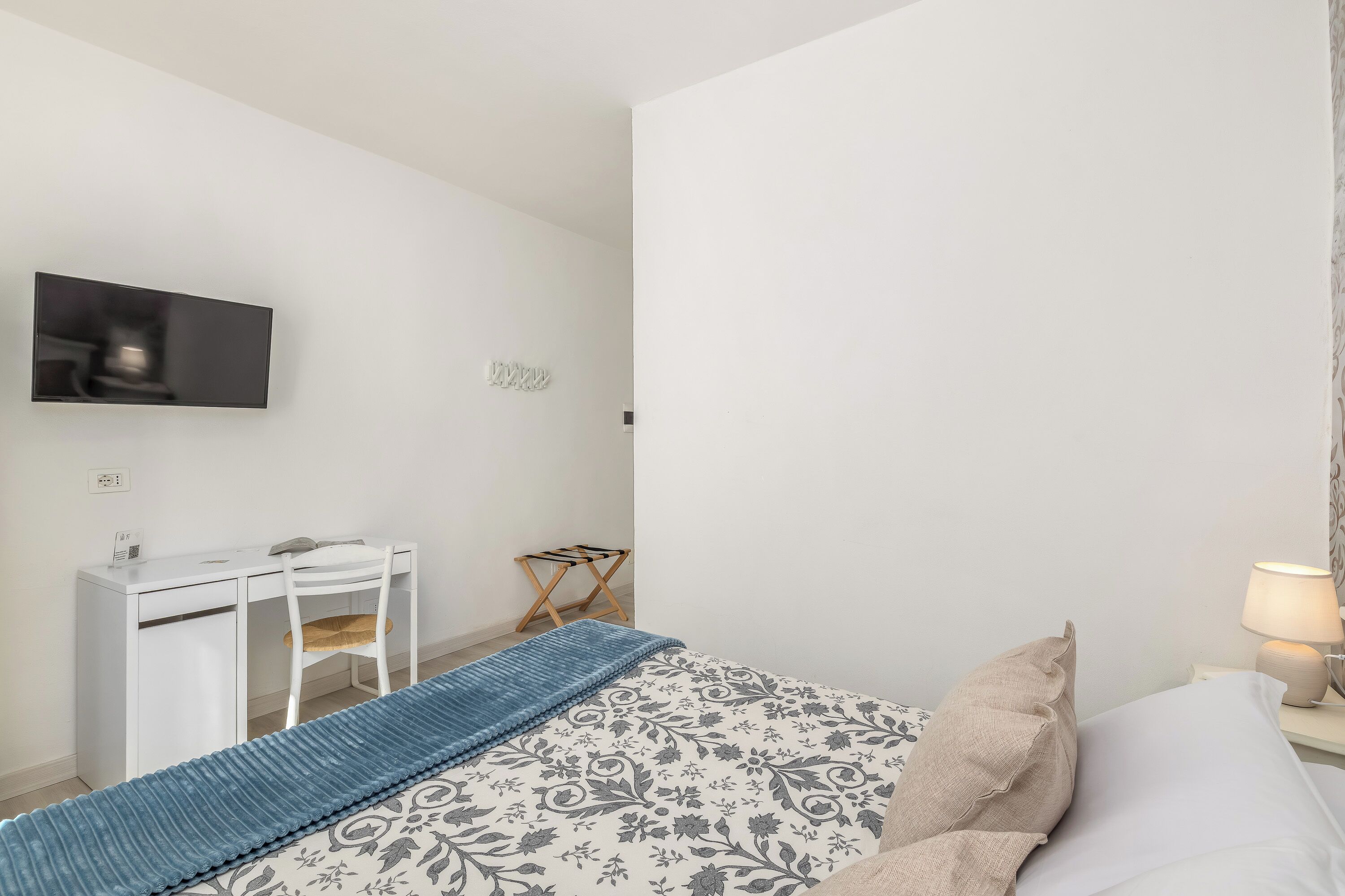 Ein Schlafzimmer mit Bett, Schreibtisch, Sessel, Wandfernseher und Nachttischlampe.