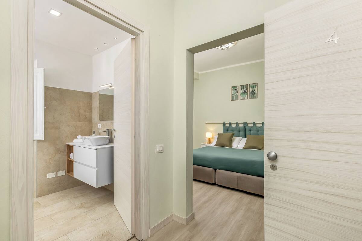 A modern bathroom with a vanity, mirror, and shower. The room features a wooden floor and a light green wall.