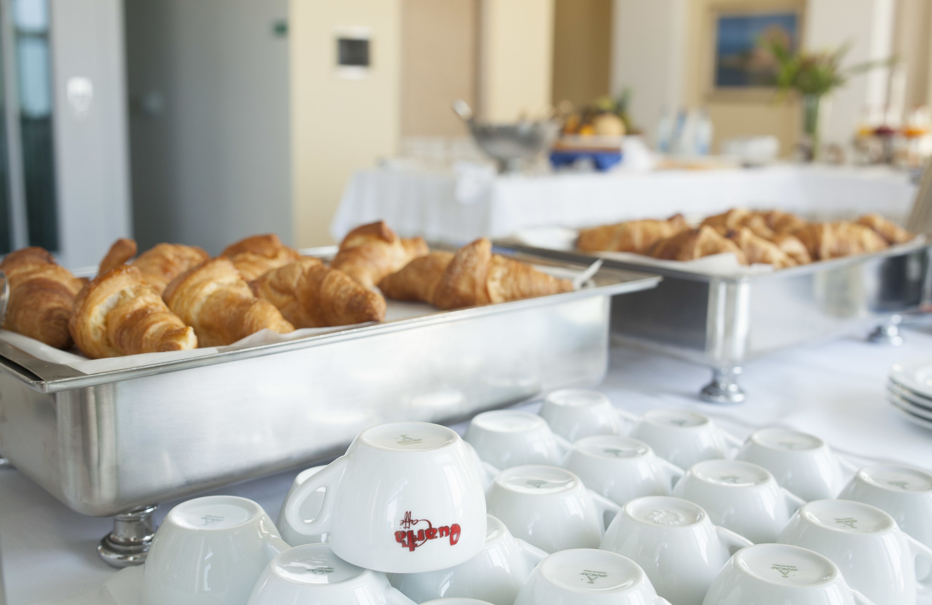 A buffet with croissants and white ceramic cups.