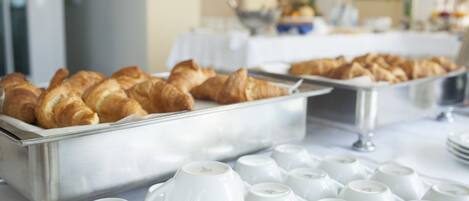 A buffet with croissants and white ceramic cups.