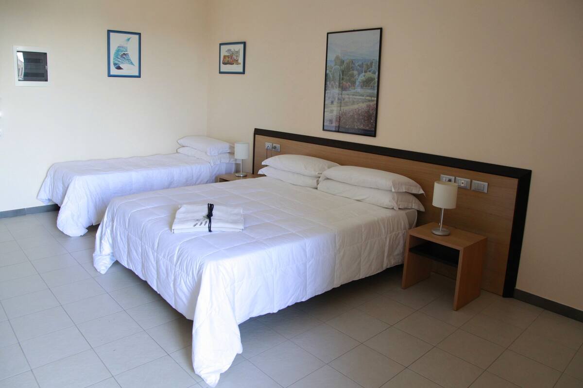 Habitació d'hotel amb dos llits, una tauleta de nit amb una làmpada i tres quadres penjats a la paret.