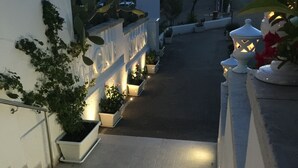 Un camí exterior ben il·luminat amb plantes en testos i un cartell de benvinguda als visitants.
