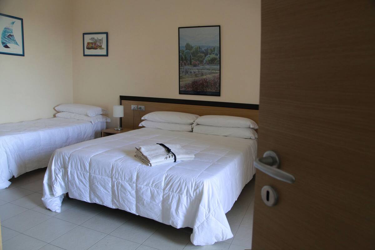 Una habitació d'hotel amb dos llits individuals, un amb capçalera de fusta i una porta amb manilla.