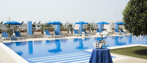 A pool area with lounge chairs and umbrellas, a table with a towel, and a well-maintained lawn.
