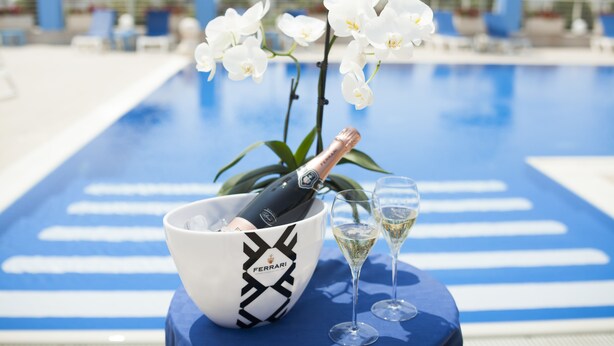 Escena a la piscina amb una ampolla de xampany en un bol, dues copes de xampany i orquídies blanques.
