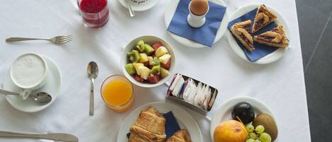 A breakfast table with croissants, fruit, a pie, and a cup of coffee.