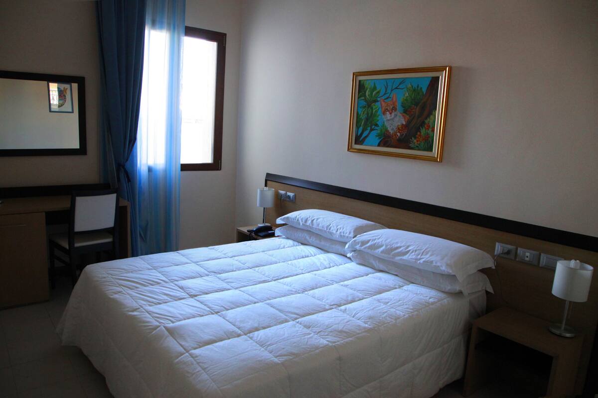 Habitació d'hotel amb un llit gran, una taula de treball, una cadira i un quadre al mur.