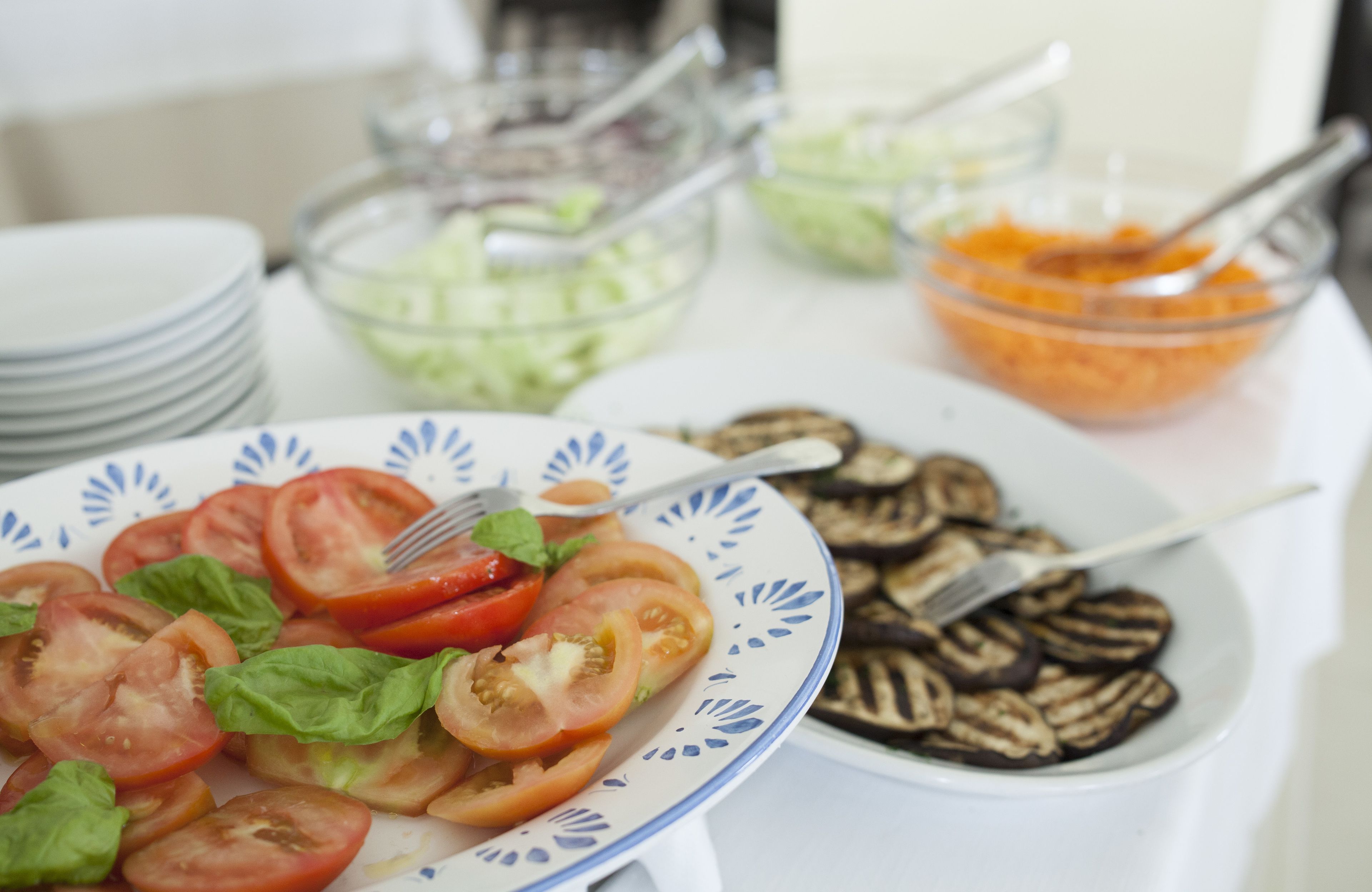 A table with a plate of sliced tomatoes and basil, a bowl of sliced cucumbers, and a bowl of orange carrots.