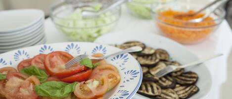 A table with a plate of sliced tomatoes and basil, a bowl of sliced cucumbers, and a bowl of orange carrots.