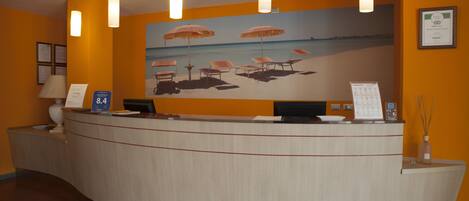 Un mostrador de recepción con un mural alusivo a la playa, un certificado enmarcado en la pared y una pantalla digital.