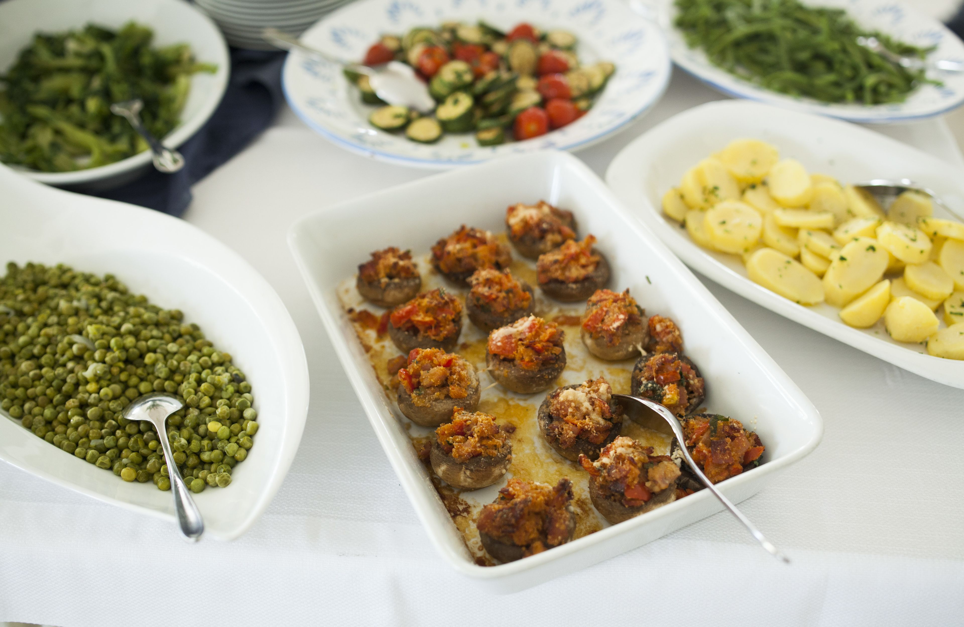 A variety of dishes including stuffed mushrooms, green peas, a salad, and sliced potatoes.