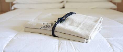 A neatly made bed with white linens and a folded towel with a dark rope tied around it.