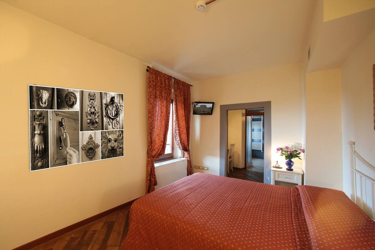A bedroom with a large bed, a wall-mounted TV, and a window with curtains.
