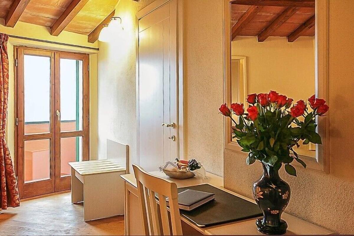 A room with a wooden table, a chair, a vase with red flowers, and a door with a view to the outside.
