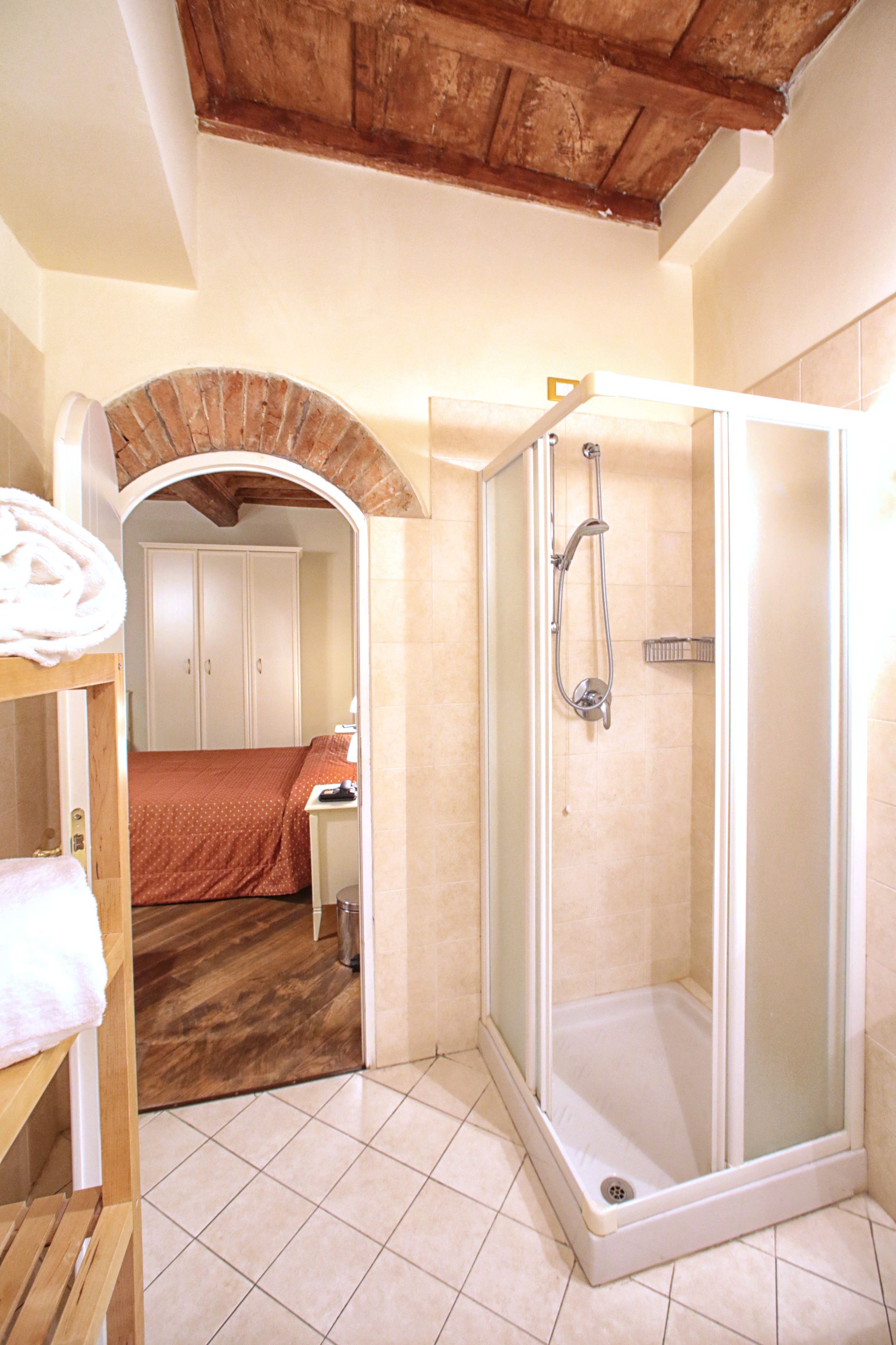 A bathroom with a shower, a wooden bench, and a bed with a red bedspread.