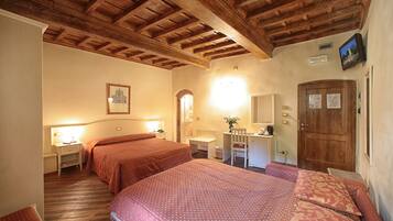 A hotel room with two beds, wooden ceiling beams, a desk with a chair, a mirror, and a door with papers on it.