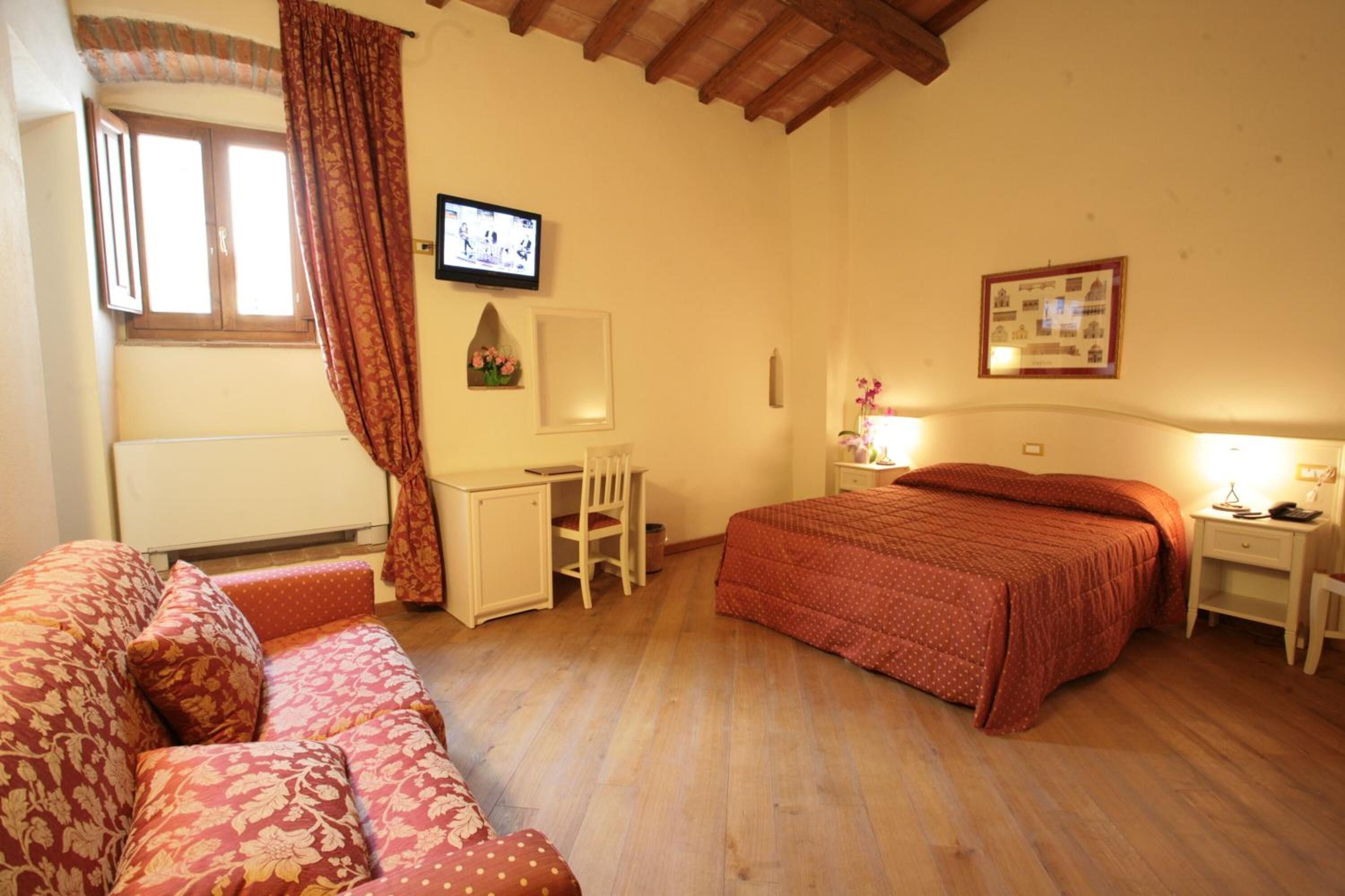 A bedroom with a bed, a desk, a chair, a TV, and a framed picture on the wall.