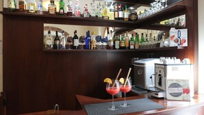 A bar area with multiple shelves of liquor bottles, a coffee machine, and two glasses of red cocktail with straws and lemon slices. - Hotel Villa S Michele (Carmignano)
