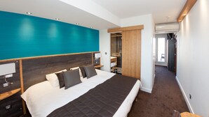 Une chambre d’hôtel moderne avec un grand lit, une tête de lit en bois, un mur d’accent de couleur turquoise et un dressing.