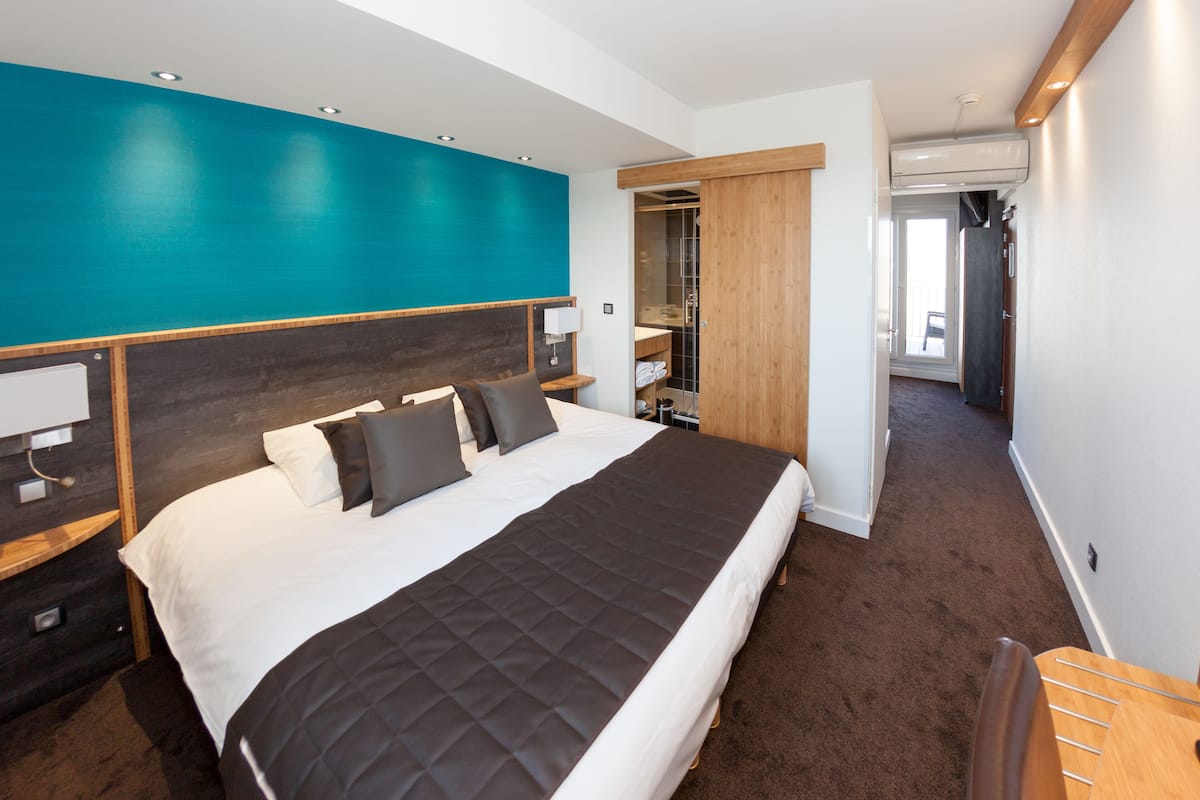 A modern hotel room with a large bed, a wooden headboard, a teal accent wall, and a walk-in closet.