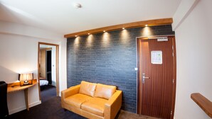 Une pièce avec un canapé en cuir, un bureau avec une lampe, un mur en briques et une porte en bois.