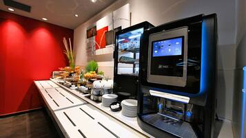 A self-service coffee station with a digital interface, a refrigerated display case, and a buffet area with various food items and condiments.