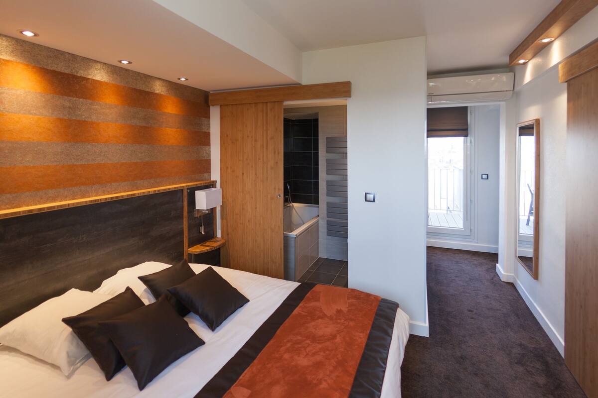 A modern hotel room with a large bed, a wooden headboard, and a view of the hallway.
