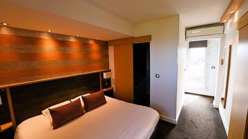 A hotel room with a bed, a headboard, a nightstand, and an air conditioning unit.
