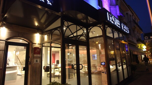 L’entrée d’un hôtel, avec une façade en verre, une enseigne ornée d’étoiles et un escalier menant à l’entrée.