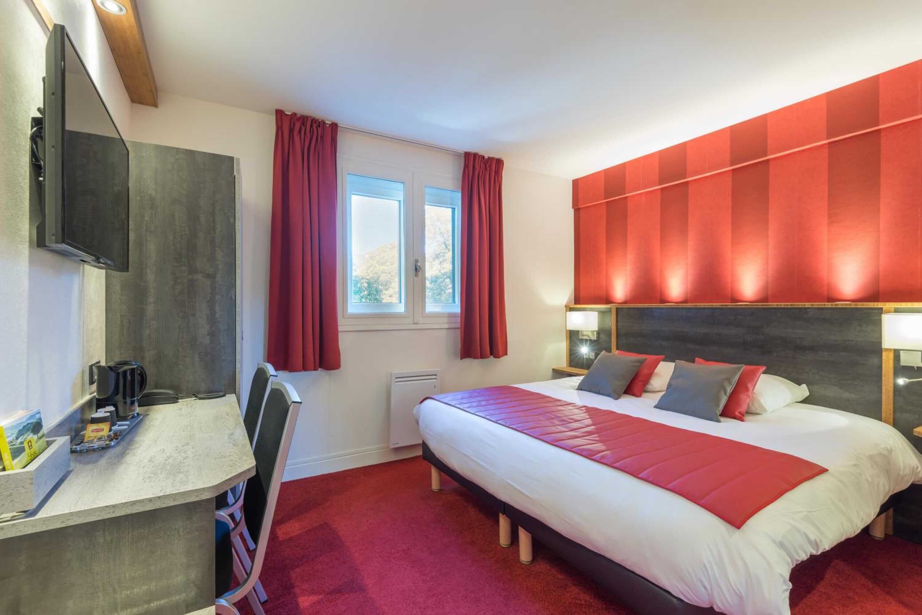 A hotel room with a bed, a desk, a chair, a TV, and a window with curtains.