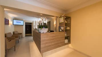 A reception area with a wooden reception desk, a large potted plant, and a TV screen displaying the Total League logo.