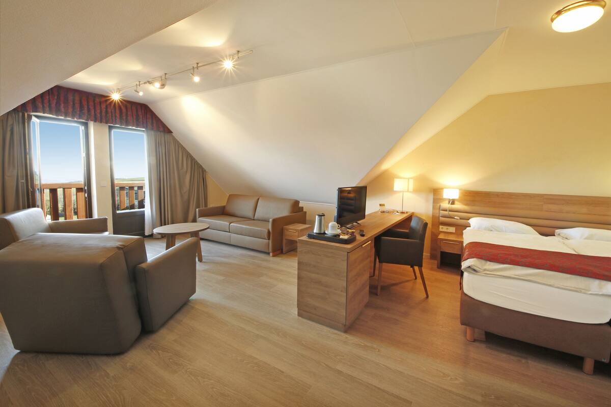Une chambre d’hôtel moderne avec un plafond mansardé, un canapé, un bureau, un lit et une vue sur l’extérieur.