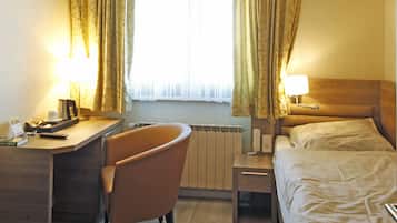 A hotel room with a desk, chair, bed, and a window with curtains.
