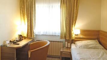 Ein Hotelzimmer mit Schreibtisch, Stuhl, zwei Betten, einem Heizkörper und Vorhängen.