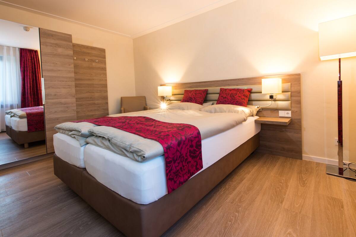 Une chambre d’hôtel moderne avec un grand lit, un plancher en bois et un miroir sur un des murs.