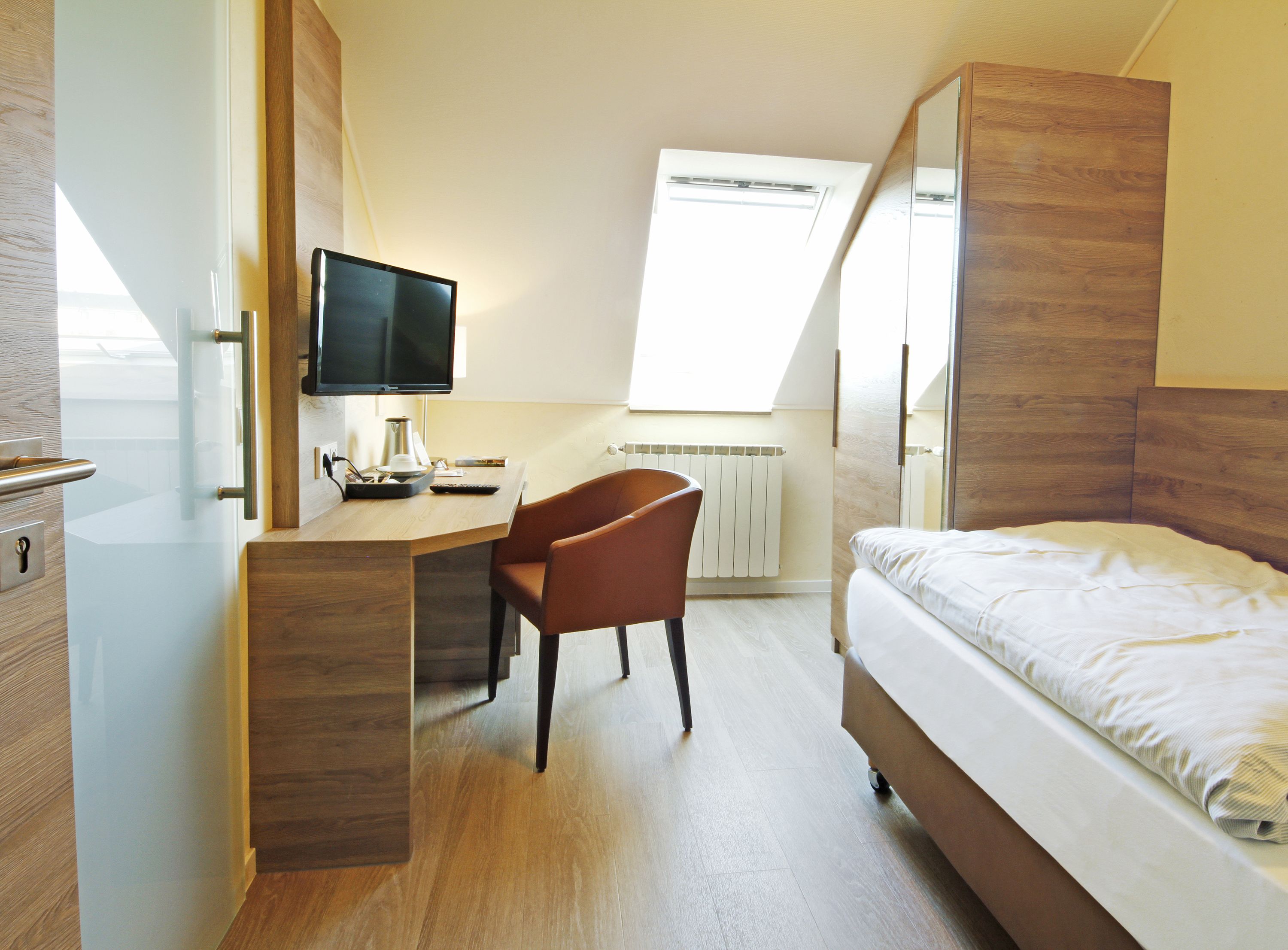 Ein Schlafzimmer mit einem Bett, einem Schreibtisch mit Stuhl, einem Fernseher und einem Fenster.