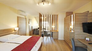 A hotel room with a bed, desk, chair, TV, and a small table with a remote control.