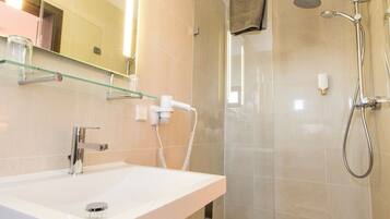 Un baño moderno con un lavamanos blanco, cabina de ducha con mampara de vidrio y un espejo grande.