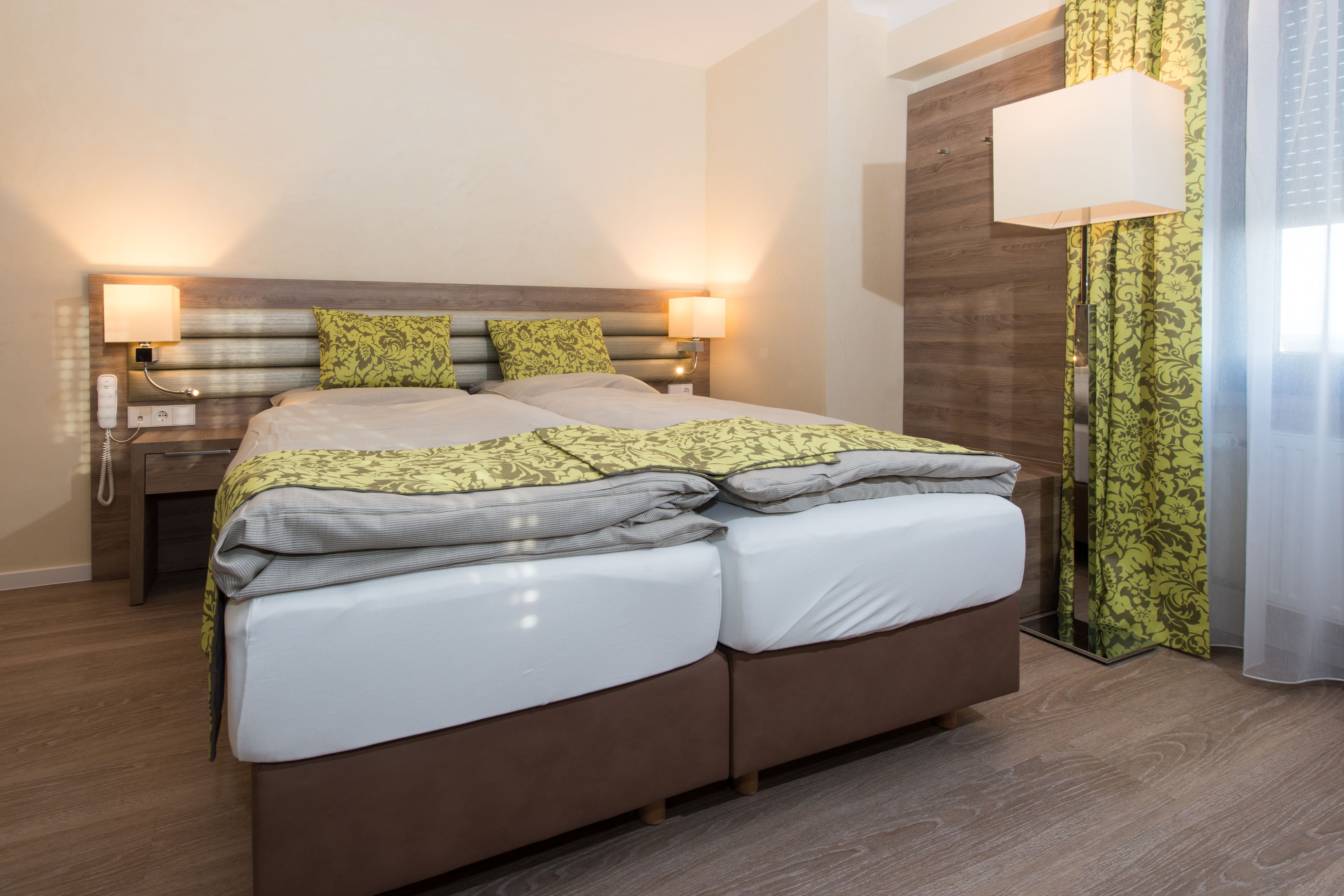 A modern hotel room with a large bed, two bedside lamps, a wooden headboard, and a nightstand with a phone.