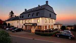 A hotel with a restaurant, multiple parked cars, and a sunset sky.
