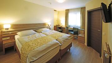 A hotel room with a double bed, a desk, a chair, a TV, and a wardrobe.
