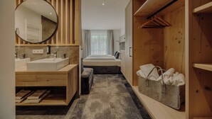 Moderni hotellihuone, jossa on puinen sisustus, suuri peili, parivuode, yöpöytä, pieni penkki, puinen vaatekaappi ja vaateteline.