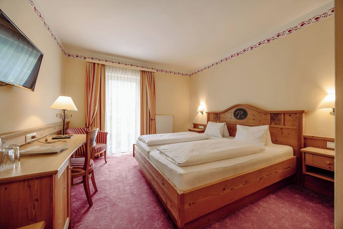 A hotel room with a wooden bed, a desk, a chair, and a television.