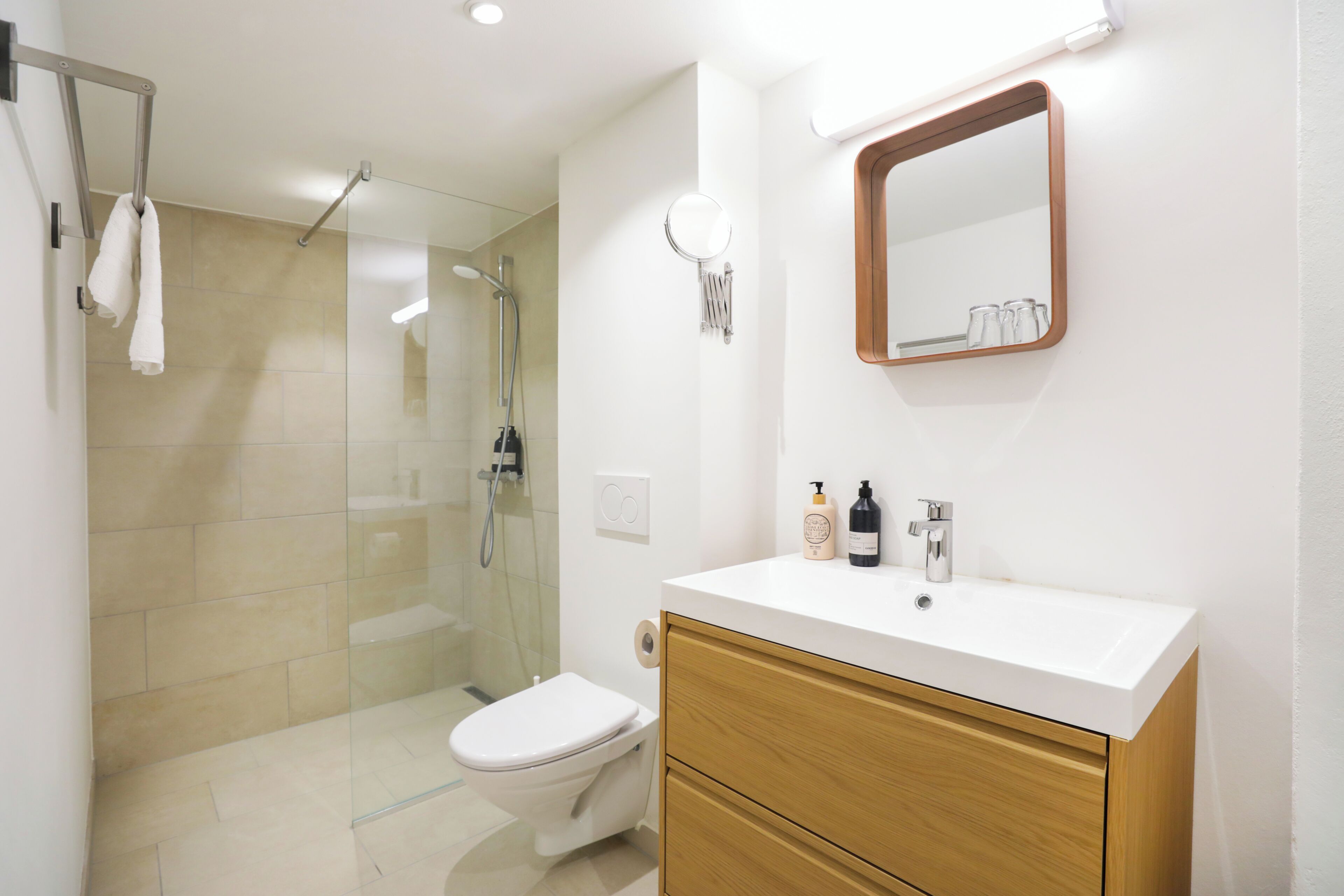 A modern bathroom with a glass shower enclosure, a white toilet, a wooden vanity with a white sink, and a mirror above the sink.