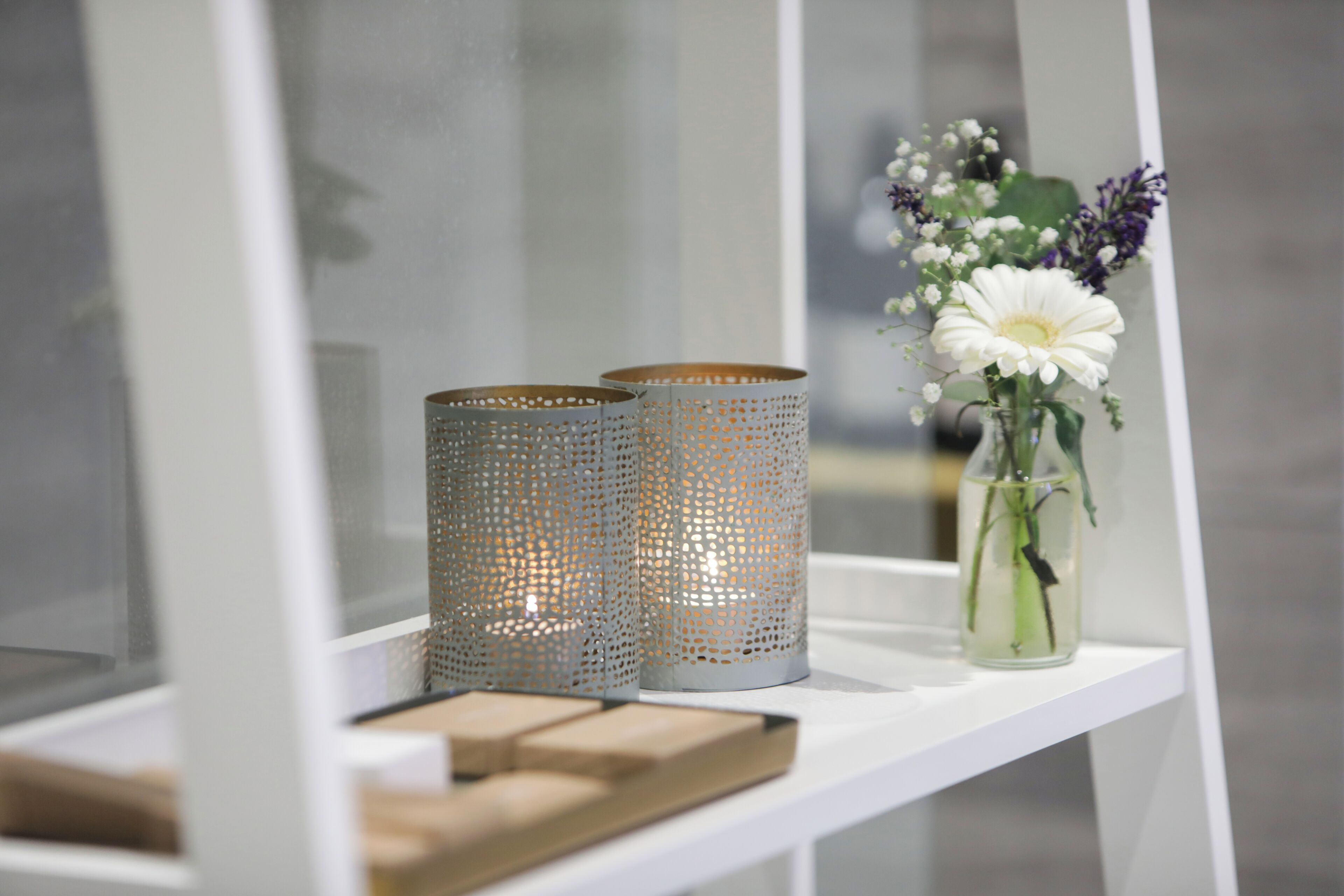 Une étagère blanche avec deux supports à bougies en métal perforé et un vase avec des fleurs.