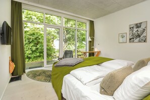 A bedroom with a large window, a bed with white linens, a green throw, and a chair.